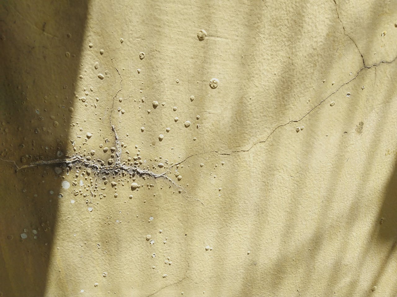 Close-up view of a textured cracked wall with shadows, showcasing decay and surface texture.